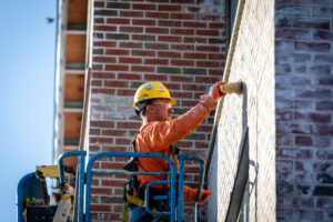BAC craftworker working safely on boom lift applying German schmear to the brick exterior of a senior living project.