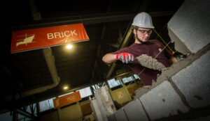 Pre-job bricklayer student spreads mortar on block at a mockup in the BAC/IMI International Training Center