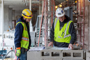 Foreman and craftworker examine project plans and documents on a job site.